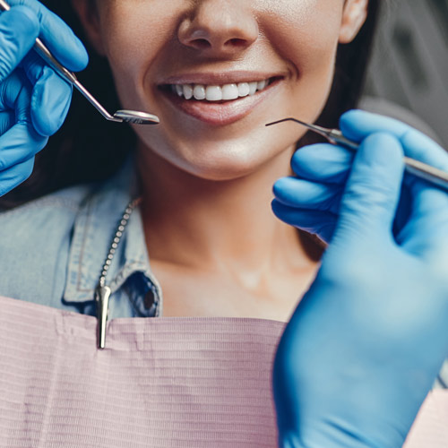 Close up of patient's mouth and doctor with gloved hands holding dental tools.