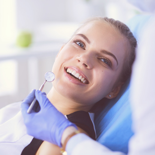 Patient sitting in a dental chair and doctor holding dental mirror in front of patient.