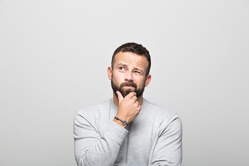 Man standing in front of white background with hand on chin and looking up.