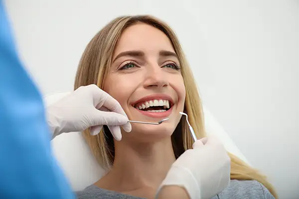 A female patient smiling during a routine dental checkup as a dentist uses dental tools to examine her teeth.