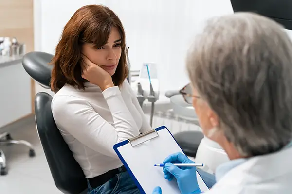 Female patient consulting with a dentist about severe tooth sensitivity during a dental appointment in a clinic. Female patient consulting with a dentist about severe tooth sensitivity during a dental appointment in a clinic.