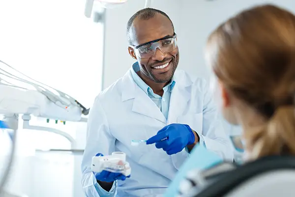 Smiling dentist explaining dental hygiene tips that can prevent bone loss to a patient using a dental model.