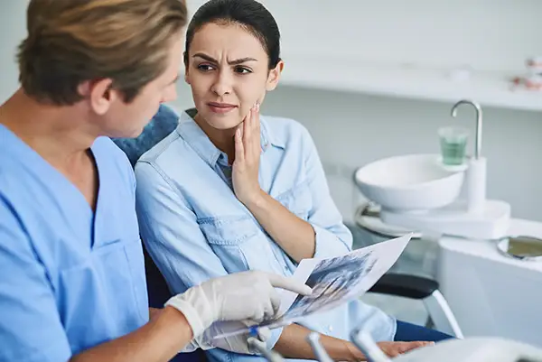 A dentist in scrubs discussing a patients sensitive tooth and treatment options.